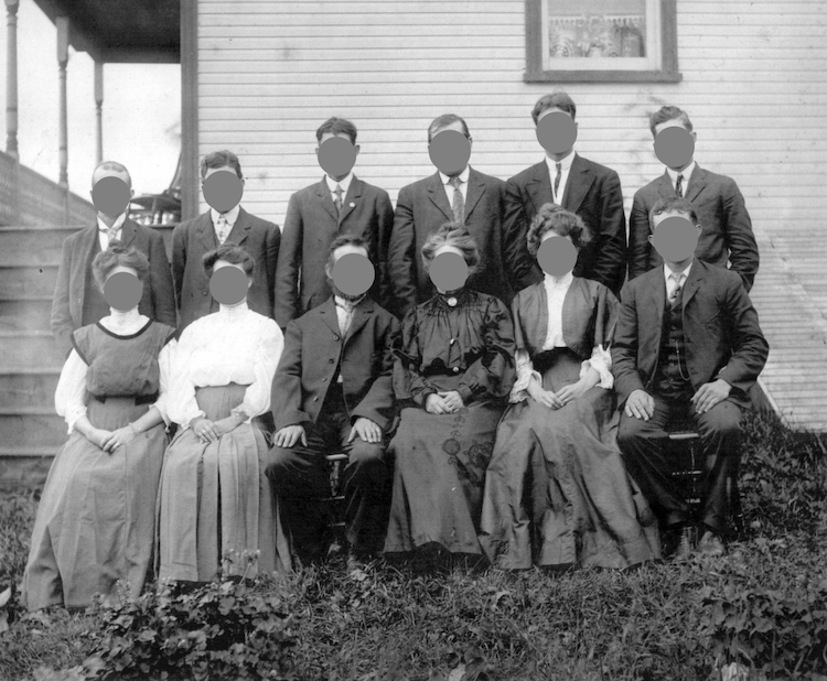 A historical photograph of twelve people sat outside a house. Thier faces have been concealed with flat grey circular masks.